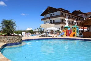 A swimming pool with lounge chairs and umbrellas, surrounded by a building with balconies and a palm tree. - Treze Tilias Park Hotel (Treze Tilias)