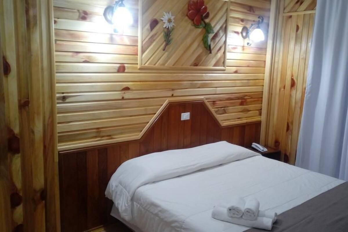 Una habitación de madera con una cama, una mesita de noche y un espejo en la pared.