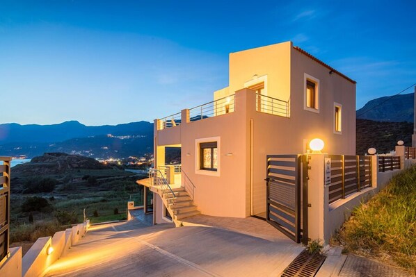 A modern two-story building with a balcony, a staircase, and a gated entrance.