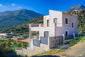A modern two-story building with a balcony, set against a mountainous backdrop.