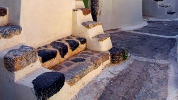 A white-washed building with a staircase leading to a door, surrounded by cobblestone pavement. - Loukas Kontos Traditional House (Santorini)