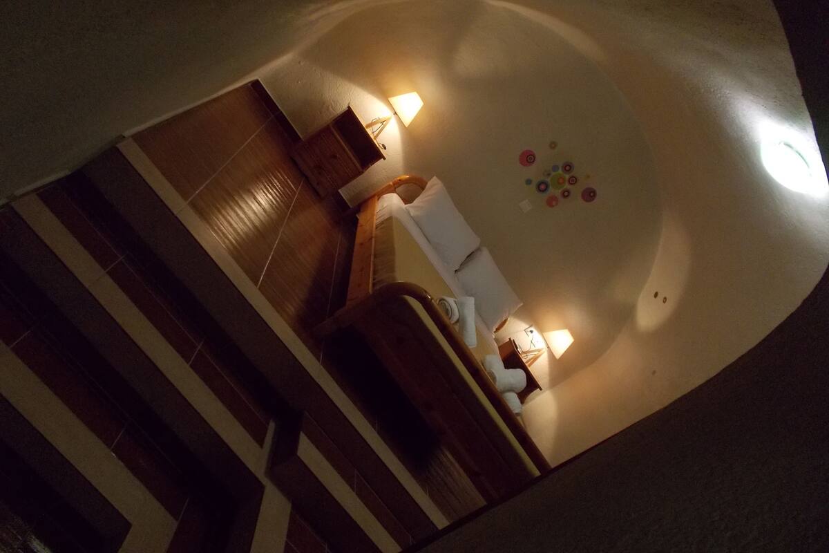 Habitació amb terra de fusta, llit amb roba de llit blanca, una petita taula de nit, una làmpada i una decoració mural.