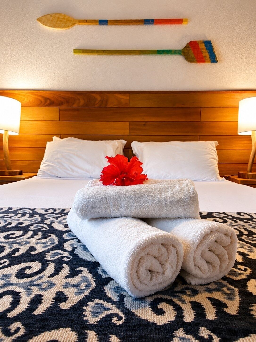 Una cama bien hecha con sábanas blancas, una flor roja decorativa y un tapete estampado.