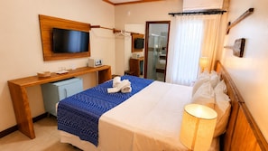 Una camera d'albergo con un letto, comodino, televisione e bagno visibile attraverso una porta aperta.