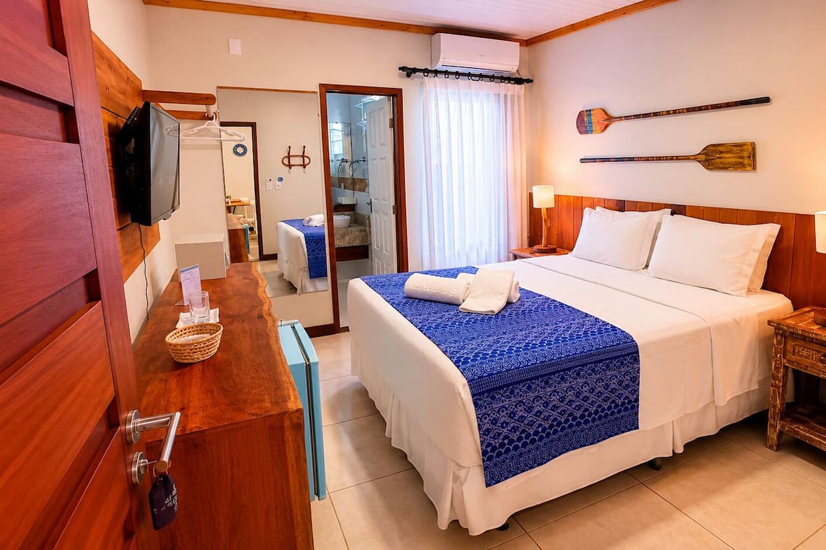 A hotel room with a bed, a wooden nightstand, a television, a mirror, and a wooden door.