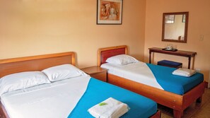 Two single beds with wooden headboards, a small bedside table with a lamp, a framed picture on the wall, and a mirror above the table. - Hotel Arrecifes (San José)