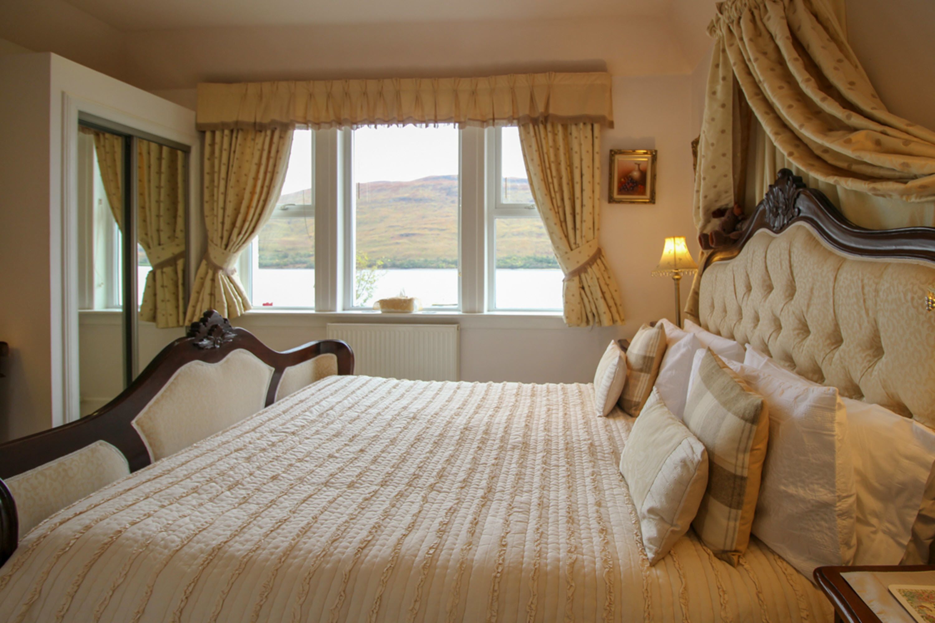 Un dormitorio con una cama grande, una ventana con cortinas, una lámpara y vistas al exterior.