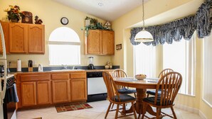 A kitchen with wooden cabinets, a dining table with chairs, a clock on the wall, and a window with curtains. - Florida Disney Vacation rental (Kissimmee)