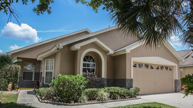 A two-story house with a beige exterior, a garage, and a well-maintained front yard with various plants and a fire hydrant. - Florida Disney Vacation rental (Kissimmee)