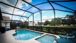 A pool area with a glass enclosure, lounge chairs, and a hot tub. - Florida Disney Vacation rental (Kissimmee)
