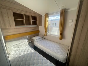 A compact RV bedroom with two bunk beds, a small table, and a window with curtains.