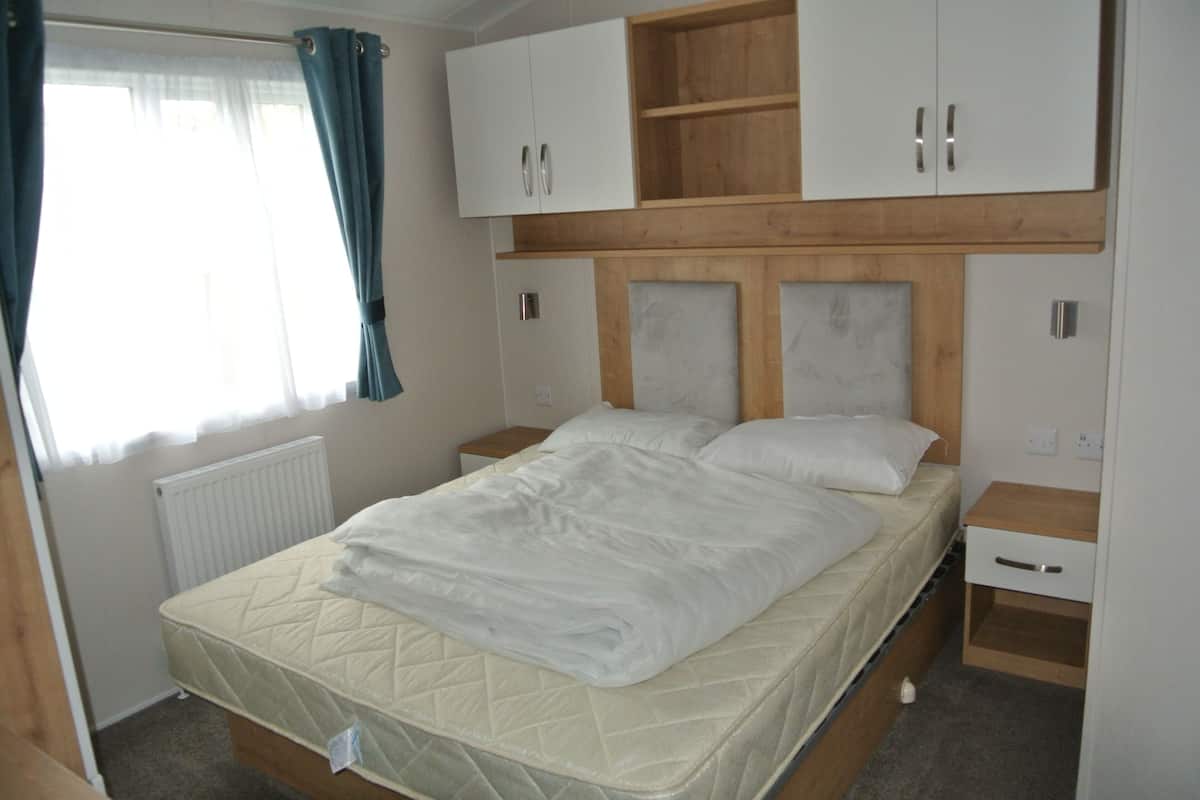 A bedroom with a bed, wooden headboard, white cabinets, and a window with curtains.