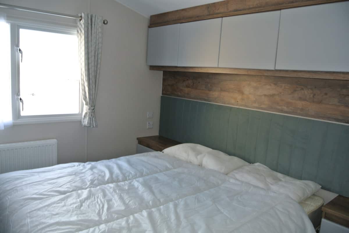 A bedroom with a bed, a window with curtains, a wooden headboard, and a white radiator.