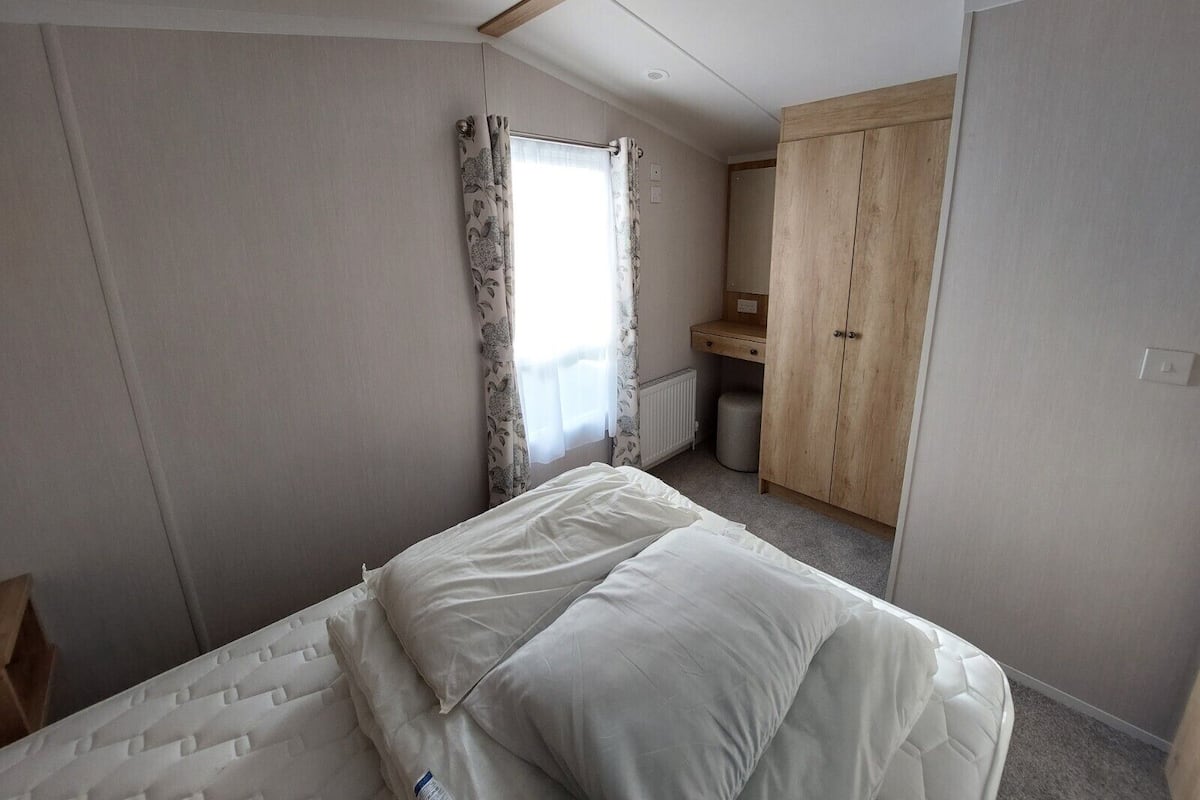 A bedroom with a bed, a wooden wardrobe, a radiator, and a window with curtains.