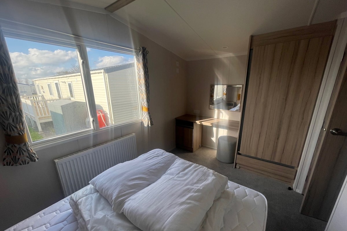 A bedroom with a bed, a desk, a mirror, and a wardrobe.