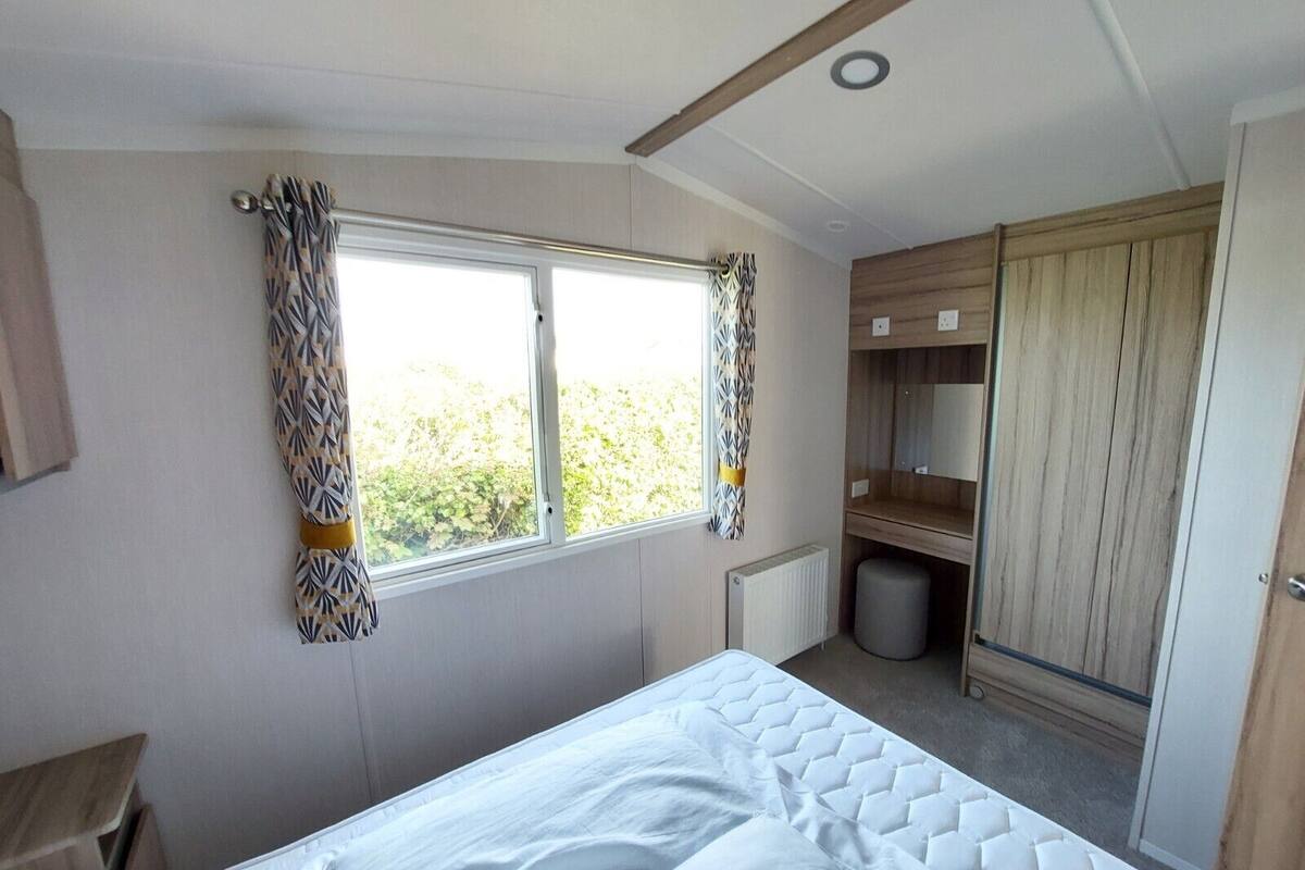 A bedroom with a bed, a window with curtains, a radiator, a waste bin, and a wardrobe.