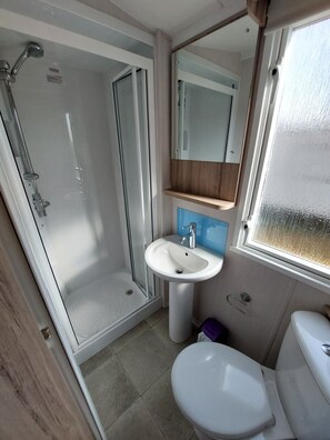 A compact bathroom with a glass shower enclosure, a pedestal sink, and a toilet.