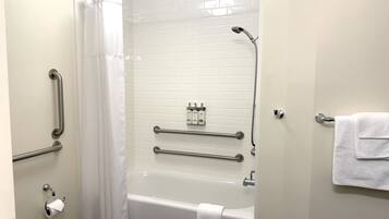 Une salle de bain équipée d’une baignoire, de toilettes, d’une douche, de barres d’appui et d’un porte-serviettes.