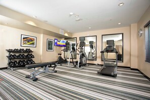 Une salle de sport d’hôtel équipée de tapis de course, d’un appareil elliptique, d’un banc de musculation et d’haltères.