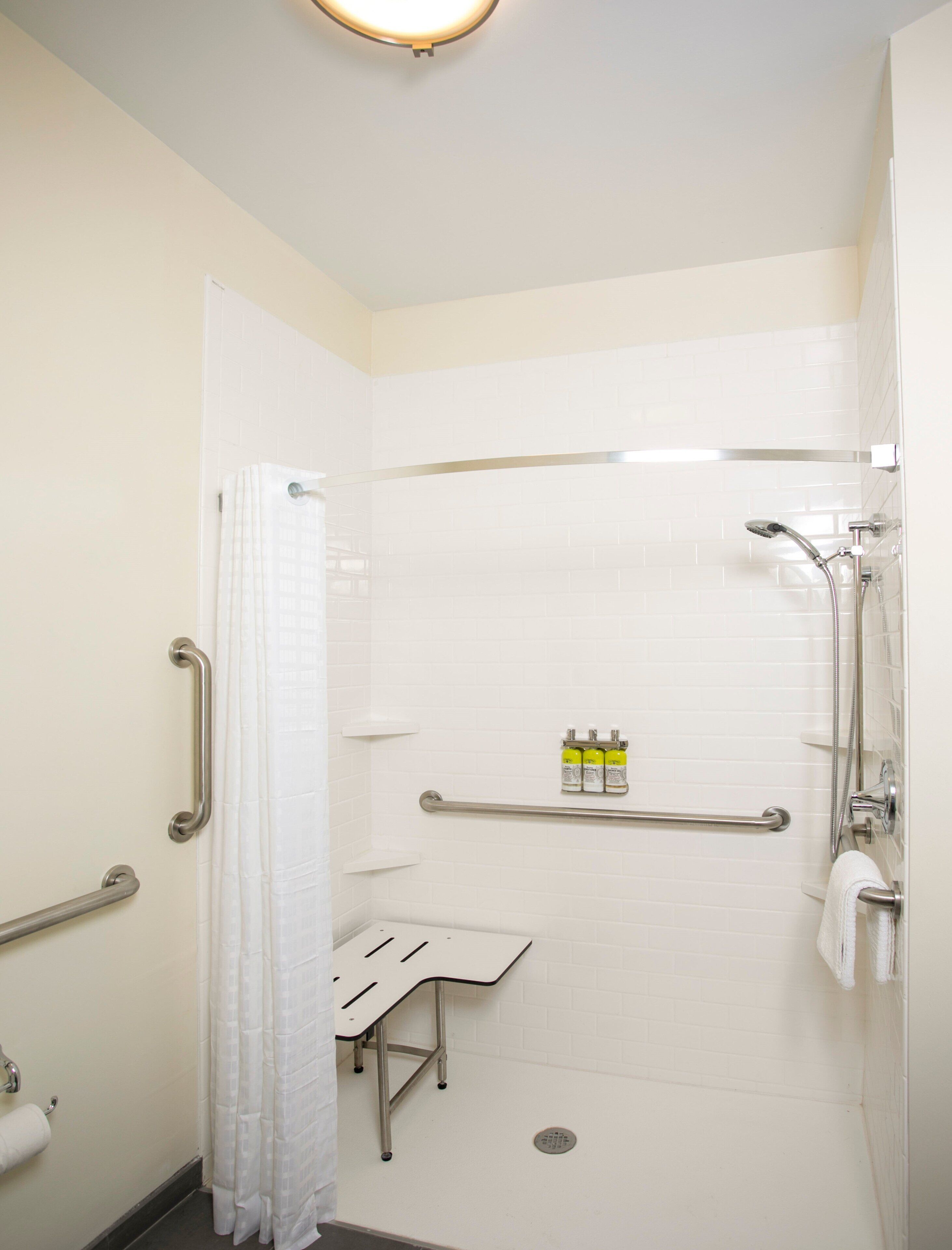 Une salle de bain équipée d’une douche, de barres d’appui, d’un porte-serviettes et d’une petite étagère contenant des articles de toilette.