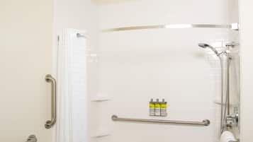Une salle de bain équipée d’une douche, de barres d’appui, d’un porte-serviettes et d’une petite étagère contenant des articles de toilette.