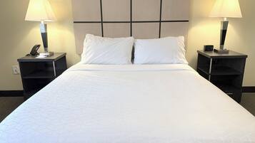 A hotel room with a large bed, two bedside tables with lamps, a headboard, and a nightstand with a clock.