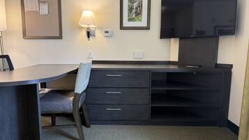 A hotel room with a desk, chair, TV, and a framed picture on the wall.