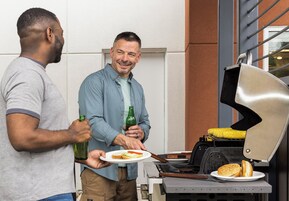 Dos personas cerca de una parrilla, con un plato de comida y una botella.