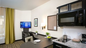 A hotel room with a dining area featuring a table, chairs, a television, a microwave, and a coffee maker. - Candlewood Suites Jacksonville - Mayport by IHG (Atlantic Beach)