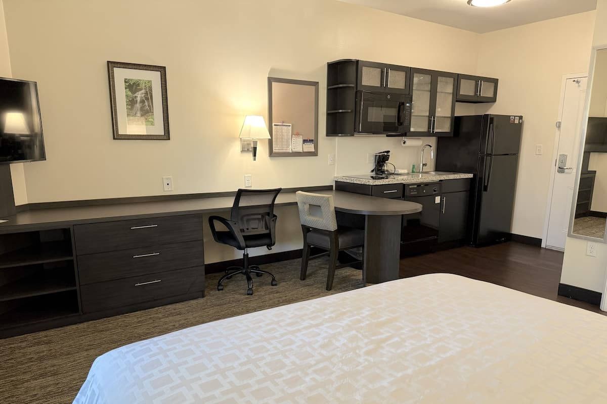 Une chambre d’hôtel équipée d’un lit, d’un bureau, d’une chaise, d’une kitchenette et d’un téléviseur.