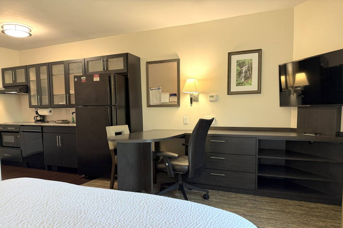 Une chambre d’hôtel équipée d’un lit, d’un bureau, d’une chaise, d’un réfrigérateur, d’un four à micro-ondes, d’un lavabo, de placards et d’une télévision.
