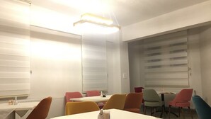 A dining area with a white table and chairs, a ceiling light, and a window with blinds. - Mengen Belediyesi Konukevi (Mengen)