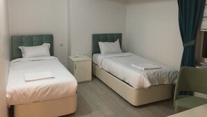 A small, clean room with two single beds, a nightstand, a chair, and a window with curtains. - Mengen Belediyesi Konukevi (Mengen)