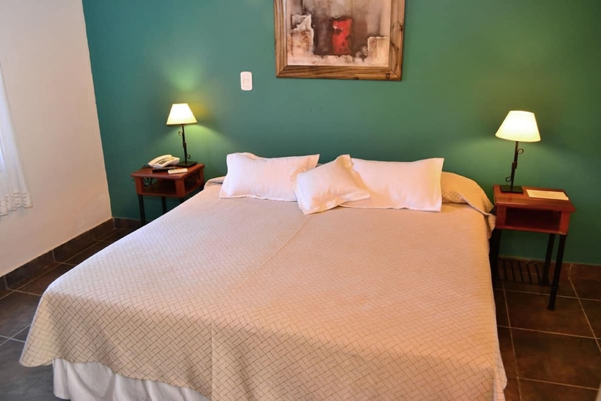 A neatly made bed with a quilted bedspread, two bedside tables with lamps, and a painting on the wall.