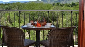 Un balcón con sillas de mimbre y una mesa preparada para el té, con vistas a un paisaje montañoso.