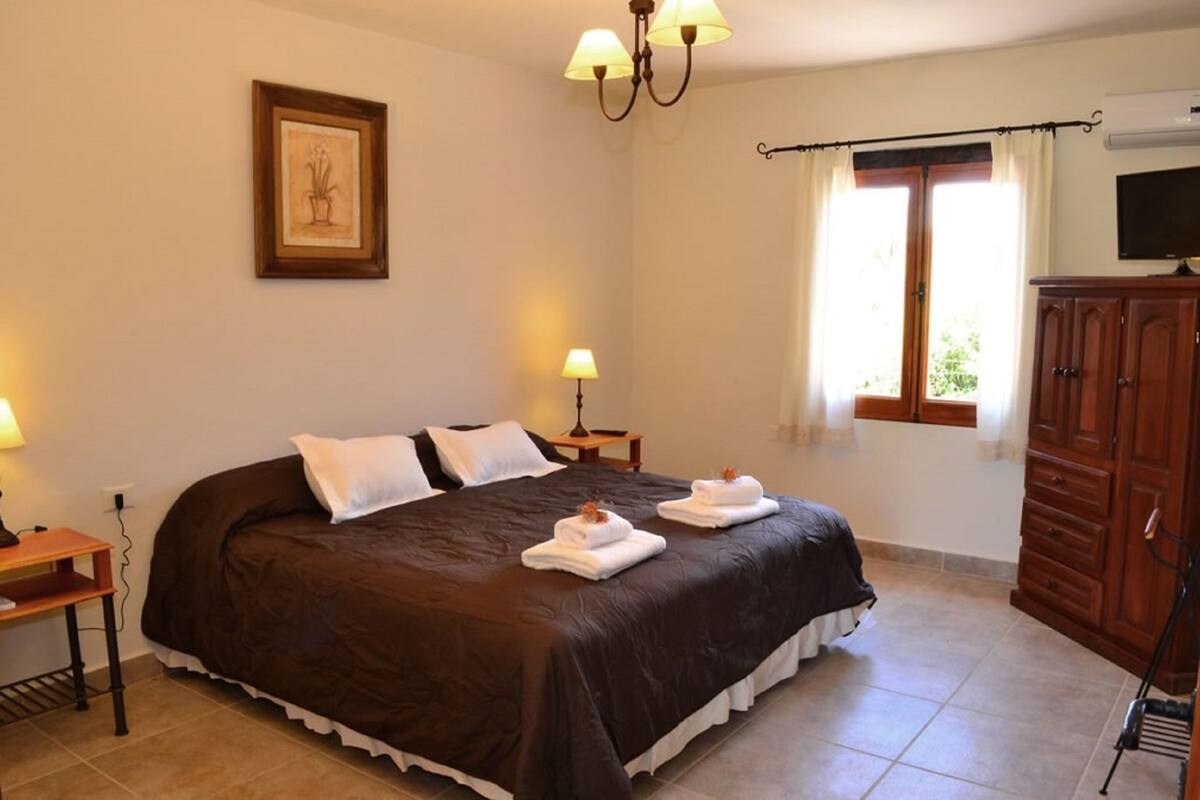A bedroom with a large bed, two bedside lamps, a wooden cabinet, and a television on the wall.