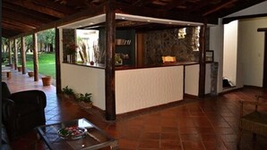 Un espacio al aire libre cubierto con pared de piedra, vigas de madera y una mesa de vidrio con un cuenco de fruta.