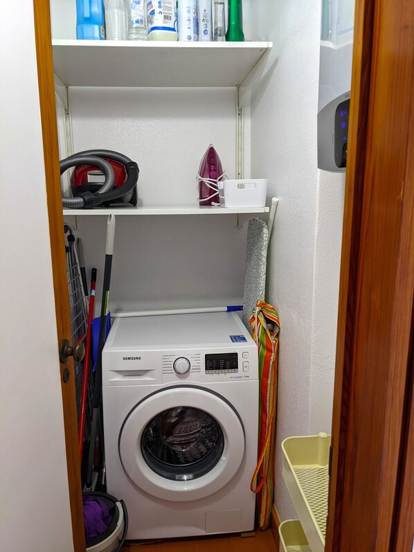A compact laundry room with a washing machine, a shelf with cleaning supplies, and a mop rack.