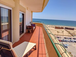 A balcony with a view of the beach, a table, chairs, and a sofa.