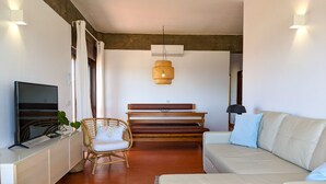 Un salon moderne comprenant un canapé, un téléviseur, un fauteuil en osier, un banc en bois et un luminaire suspendu.