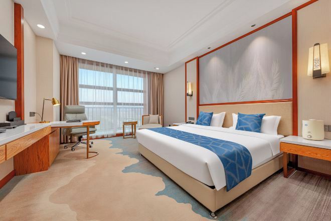 A hotel room with a large bed, a desk, a chair, a TV, and a window with curtains.
