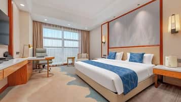 A hotel room with a large bed, a desk, a chair, a TV, and a window with curtains.