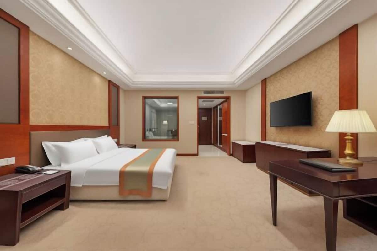A hotel room with a bed, a desk, a TV, and a lamp.