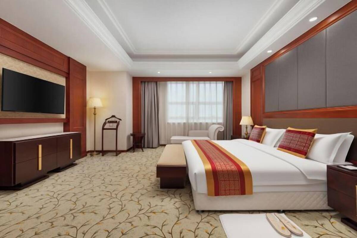 A hotel room with a large bed, a TV, a desk, and a chair.