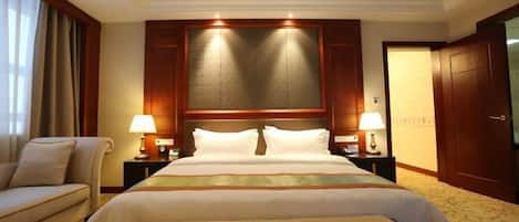 A hotel room with a large bed, two bedside tables with lamps, a sofa, and a wooden door.