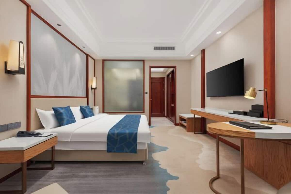 A hotel room with a bed, desk, chair, and a TV on the wall.