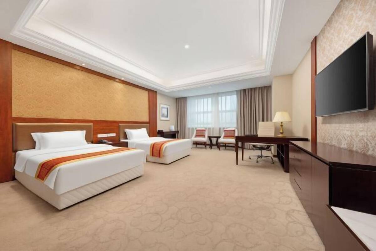 A hotel room with two beds, a desk, a chair, a TV, and a large window.