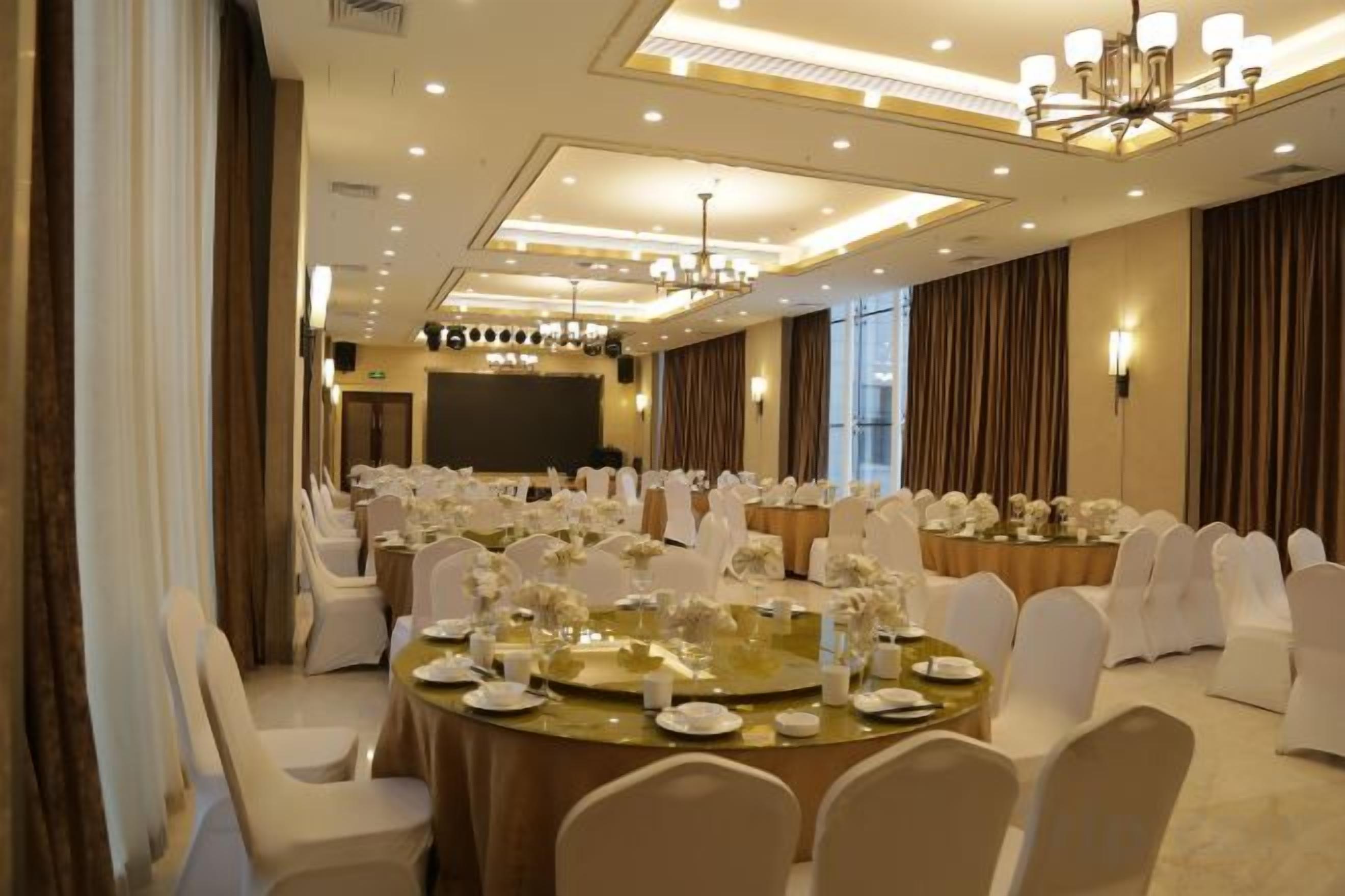 A banquet hall with round tables set for dining, white chairs, and a stage in the background.