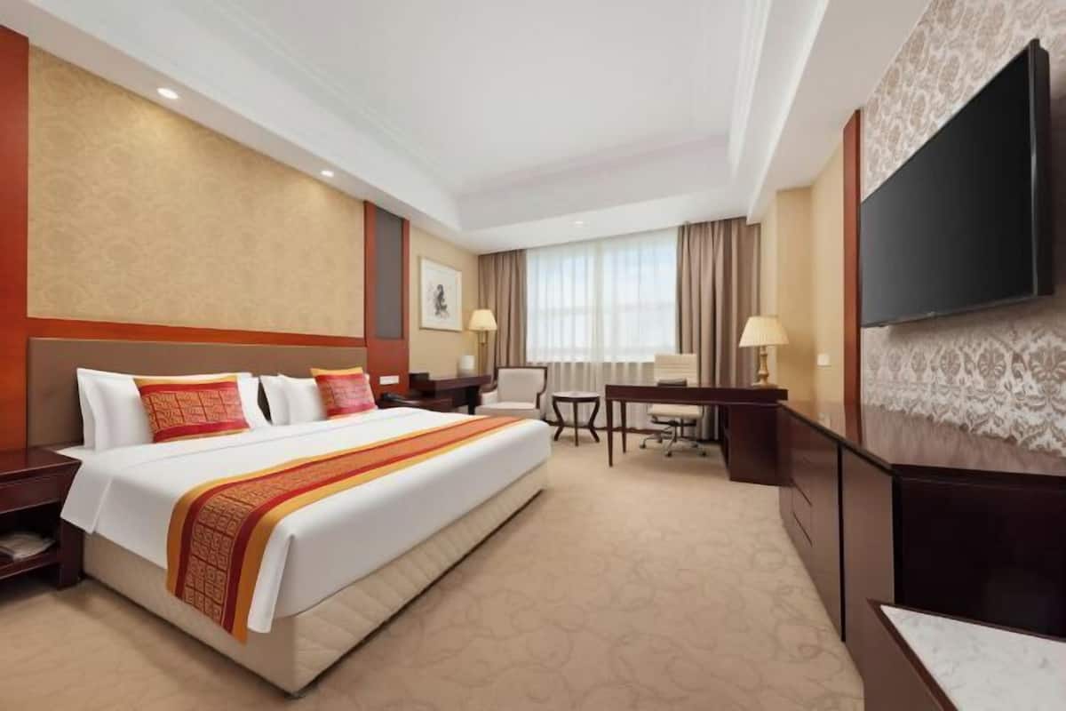 A hotel room with a large bed, a desk, a chair, a TV, and a window with curtains.