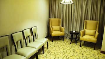 A hotel room with a seating area, two armchairs, a small table, and a patterned carpet.